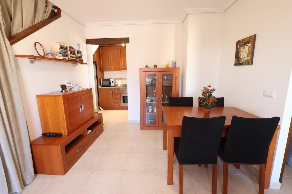 Dining and living area with a wooden table and chairs, a TV cabinet, and a view of the kitchen.