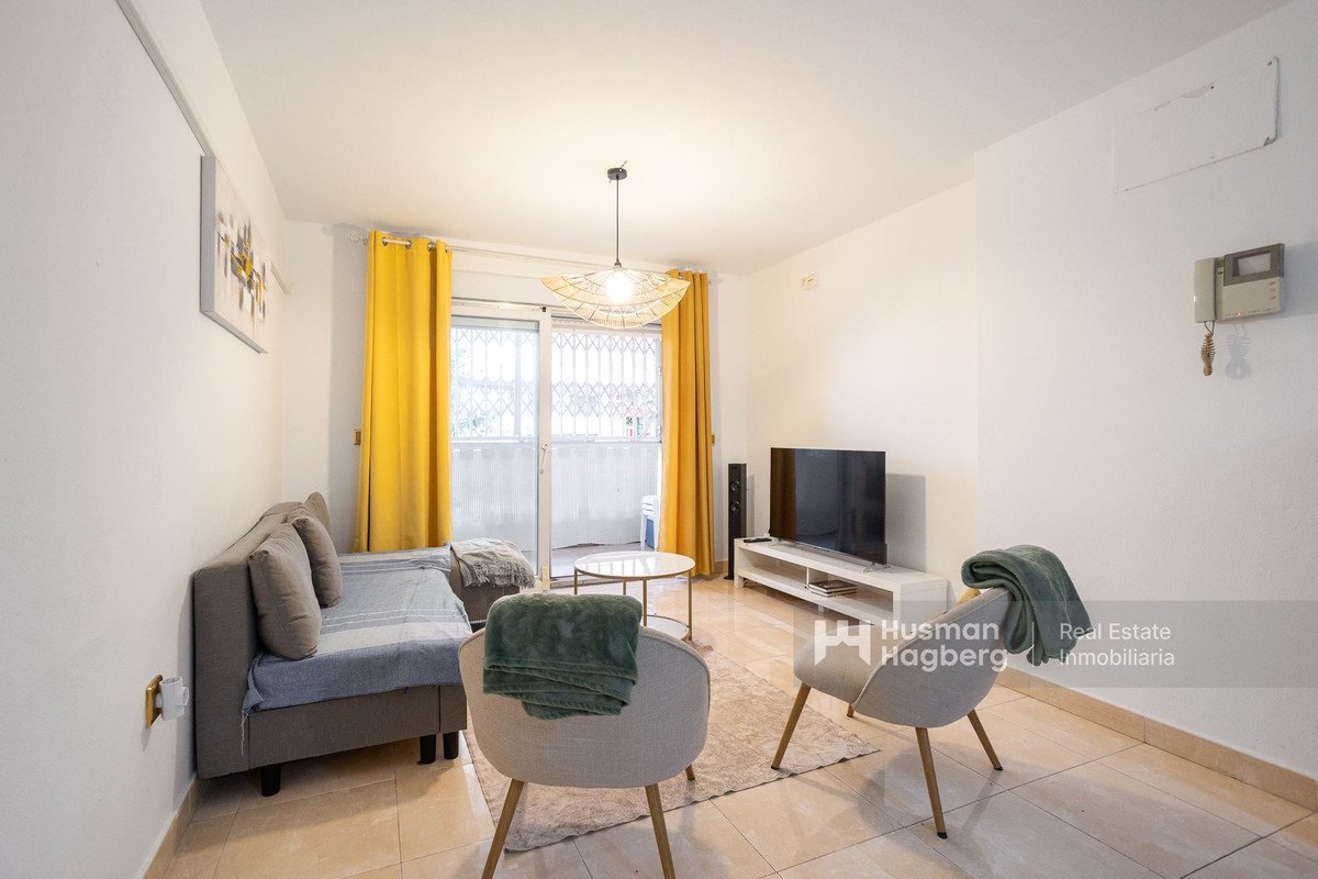 Bright living room with yellow curtains, sofa, chairs, and a TV.