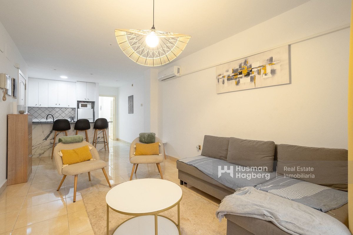 Modern living room with open-plan kitchen, sofa, chairs, and pendant light