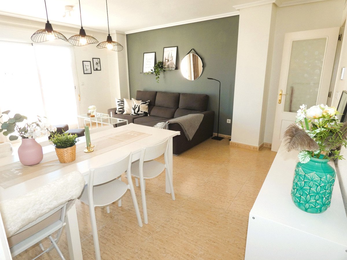A modern dining and living area with a white table, gray sofa, and decorative accents.
