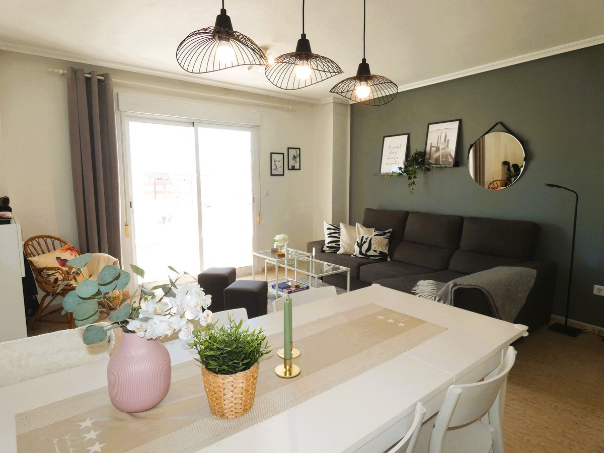 Modern living and dining room with dark sofa, white table, plants, and large window. Decorated with framed art and a round mirror.