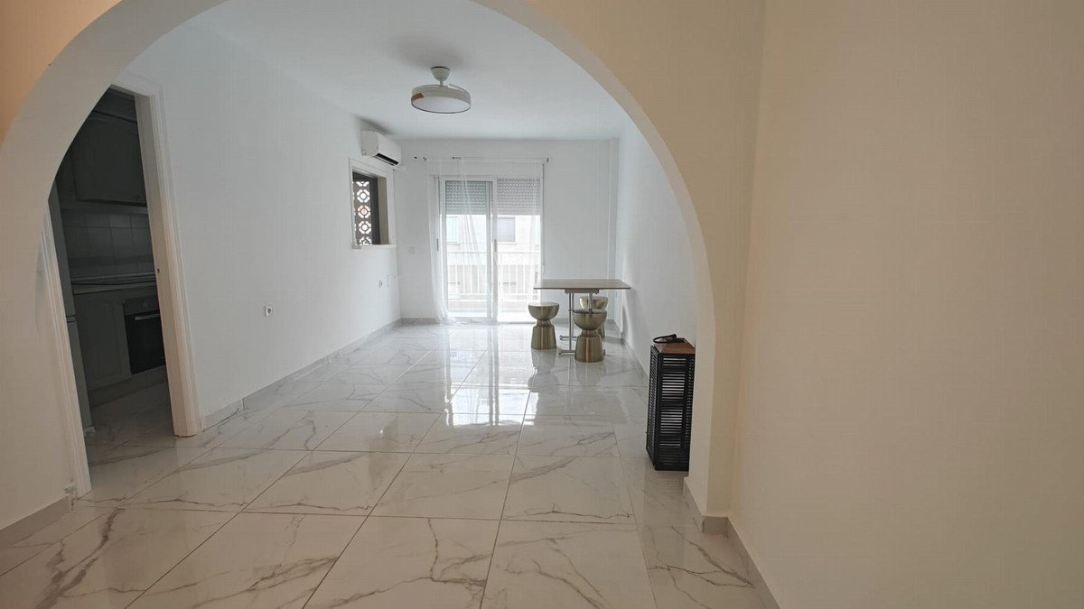 A bright living area with a kitchenette, marble floors, and access to a balcony with a small table and stools.