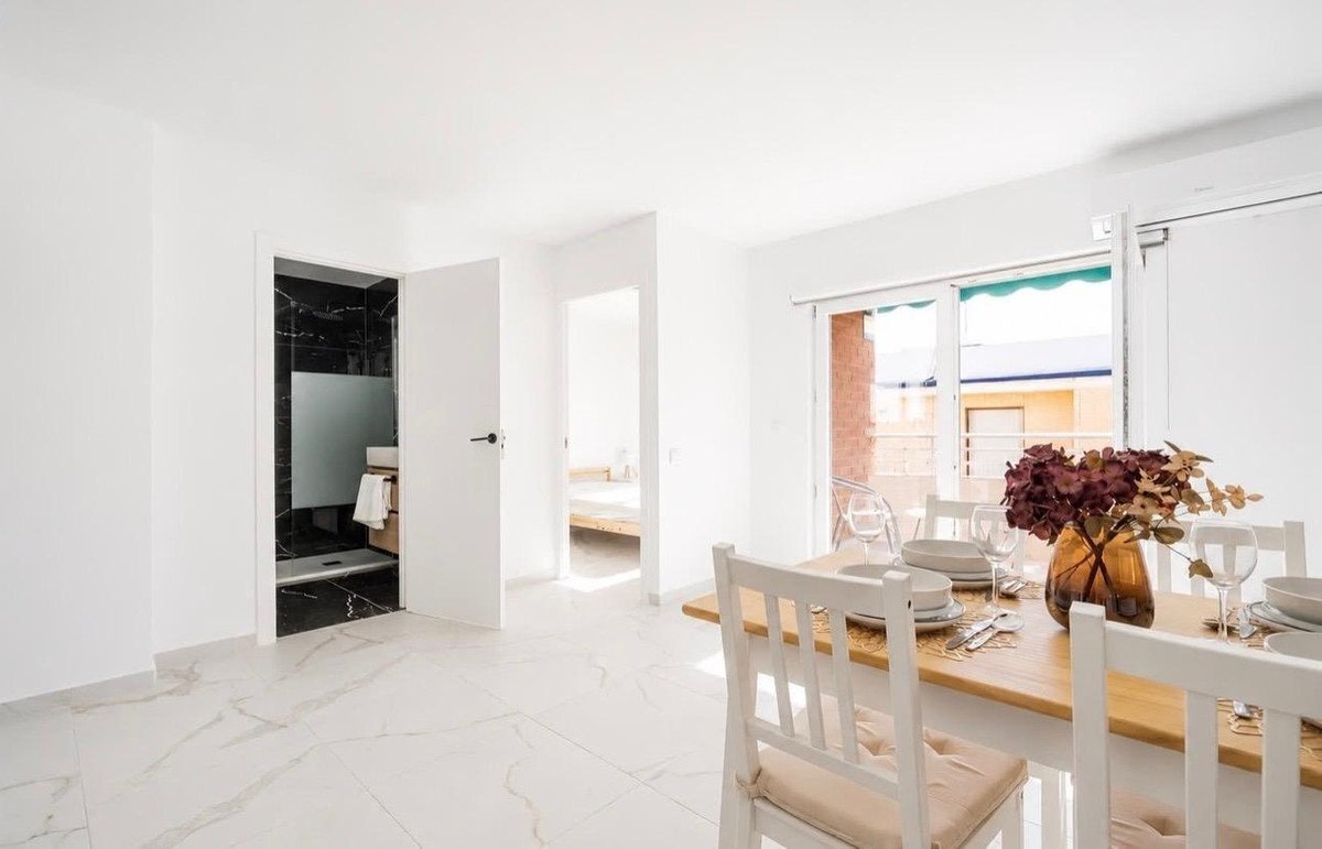 Modern dining area with a wooden table set for a meal, featuring a view to the balcony and access to a stylish bathroom.