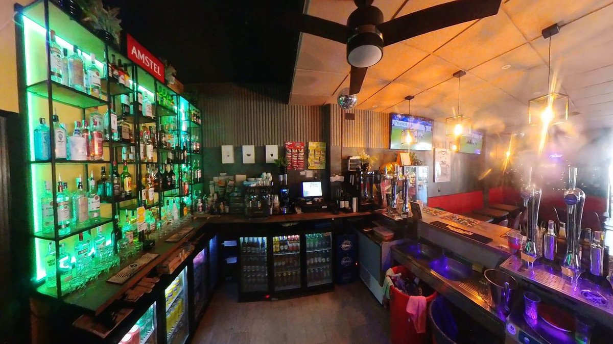 A well-stocked bar with ambient green and purple lighting, multiple beer taps, and televisions on the wall.