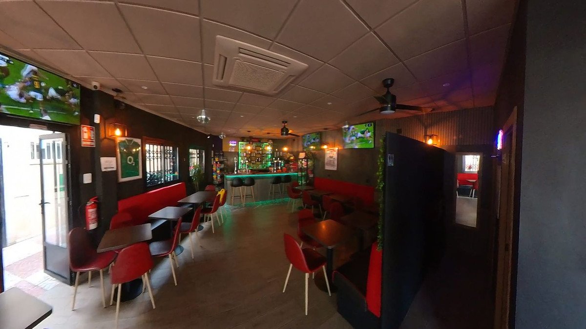 Modern bar interior with a long illuminated bar, seating booths, tables, chairs, and screens showing sports.