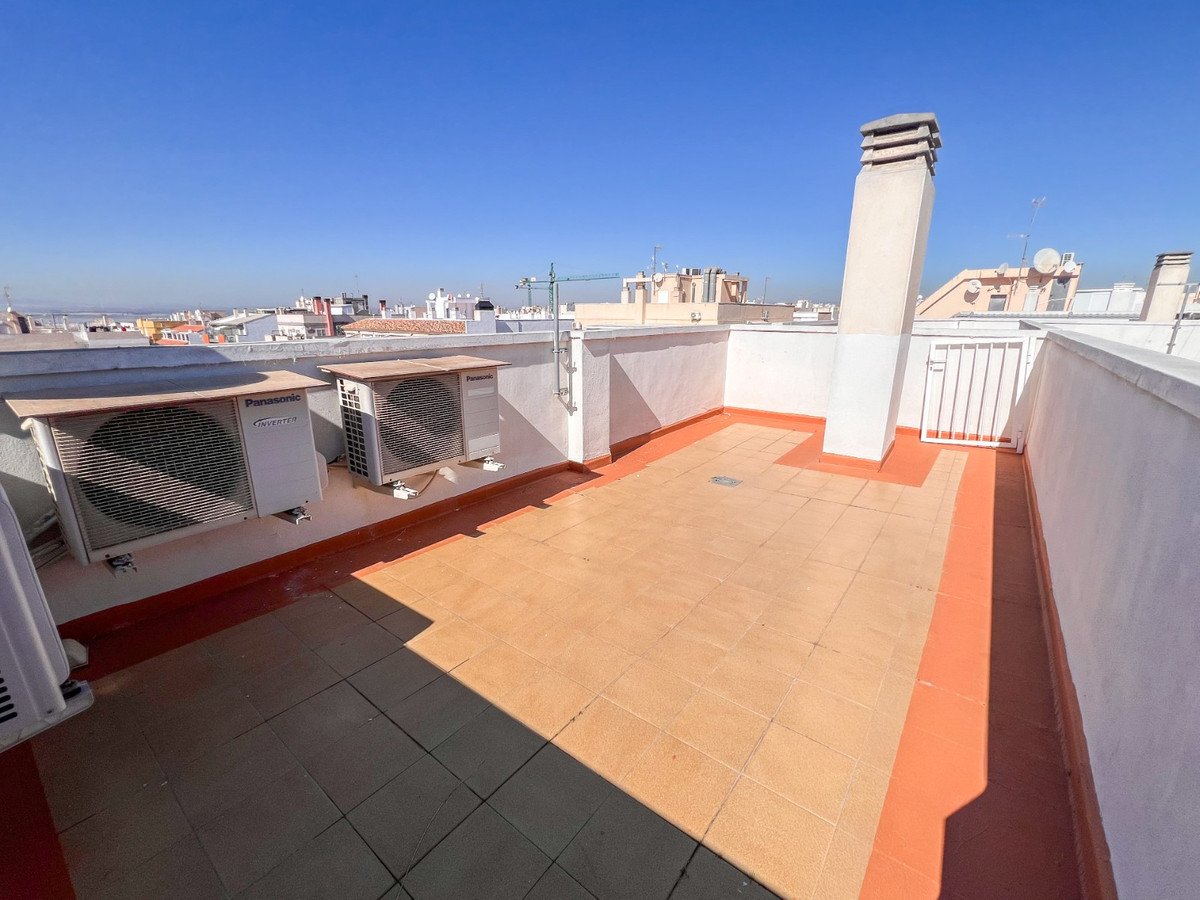 A tiled terrace with air conditioning units and a chimney, offering views of the city rooftops under a clear blue sky.