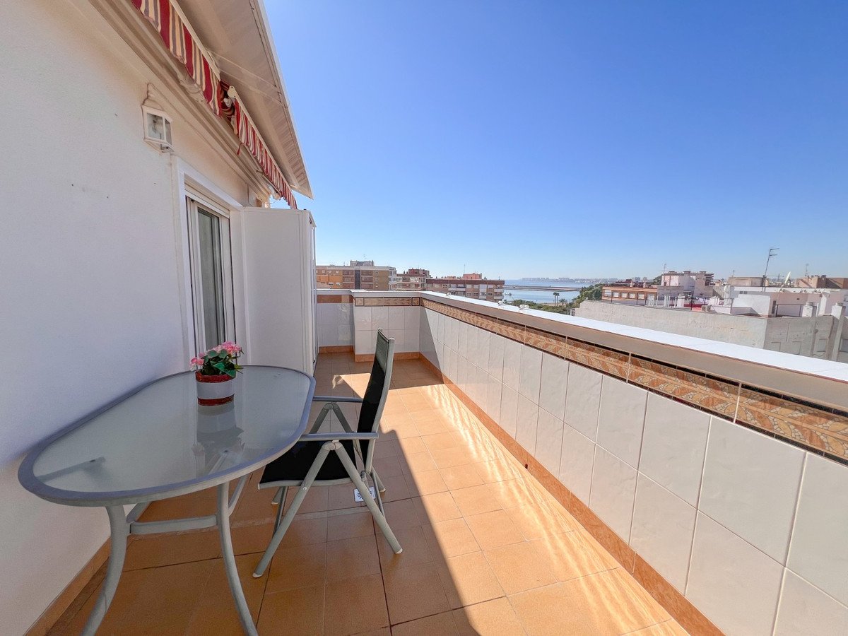 Balcony with glass table, chair, and sea view under clear blue sky.