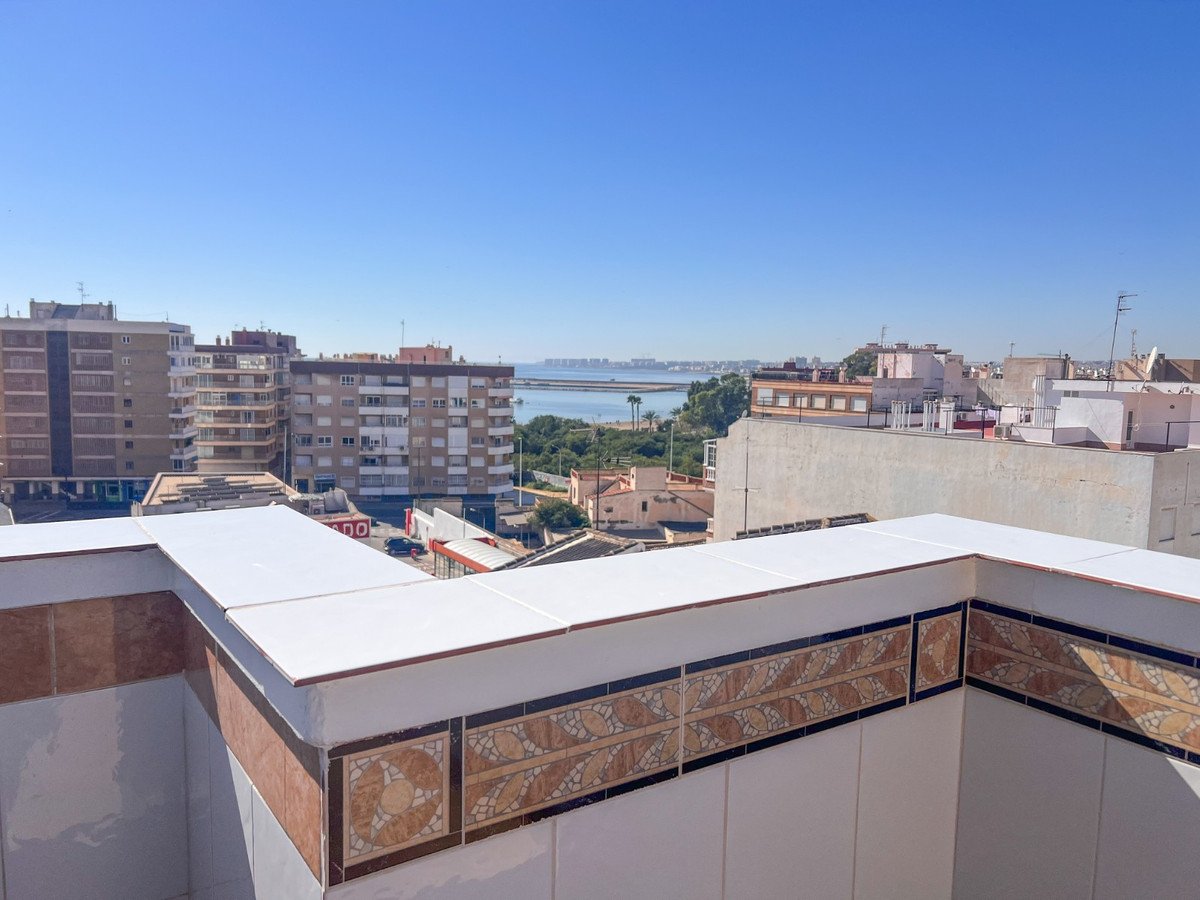 Balcony view of coastal city with sea, buildings, and clear blue sky.