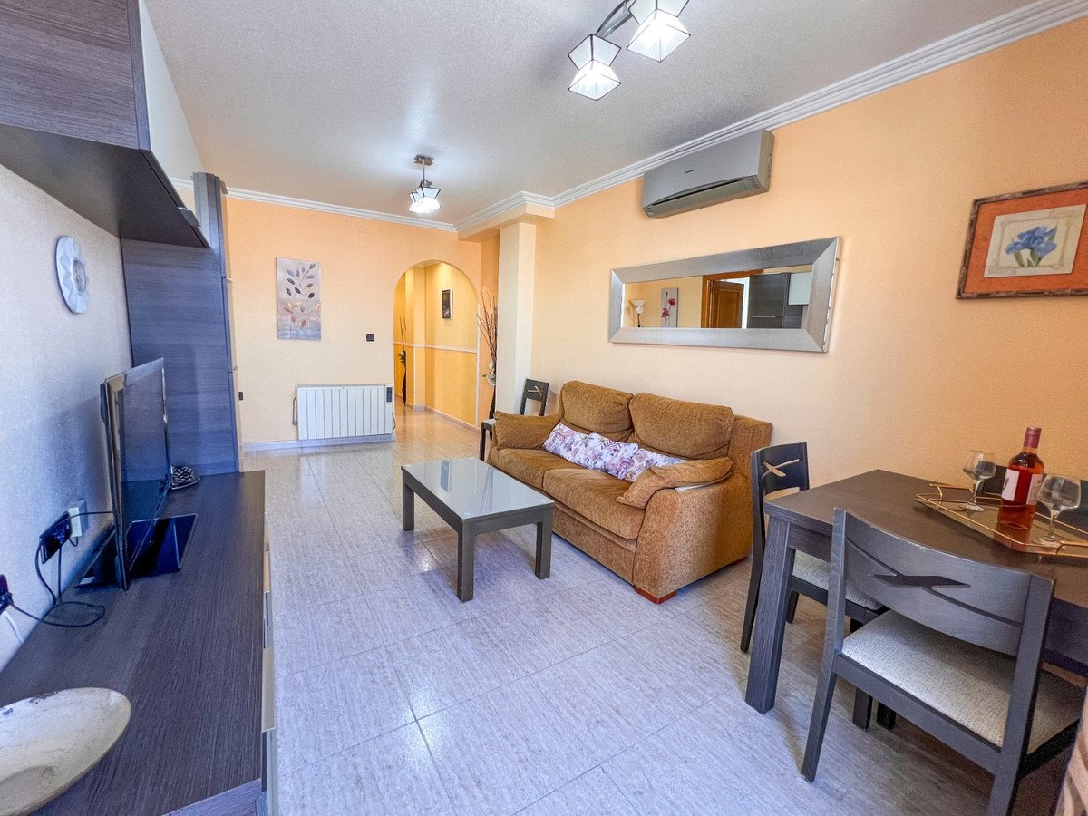 Living room with brown sofa, glass coffee table, dining set, TV, and air conditioning.