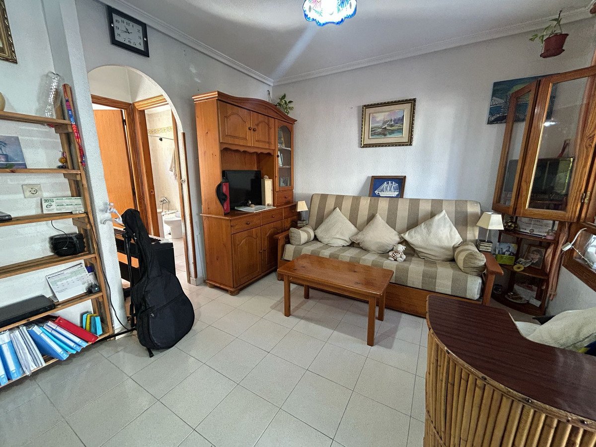 Living room with striped sofa, wooden furniture, tiled floor, and arched doorway to bathroom.