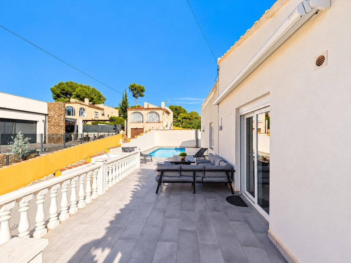 Spacious patio with outdoor seating area overlooking a swimming pool and surrounding houses.