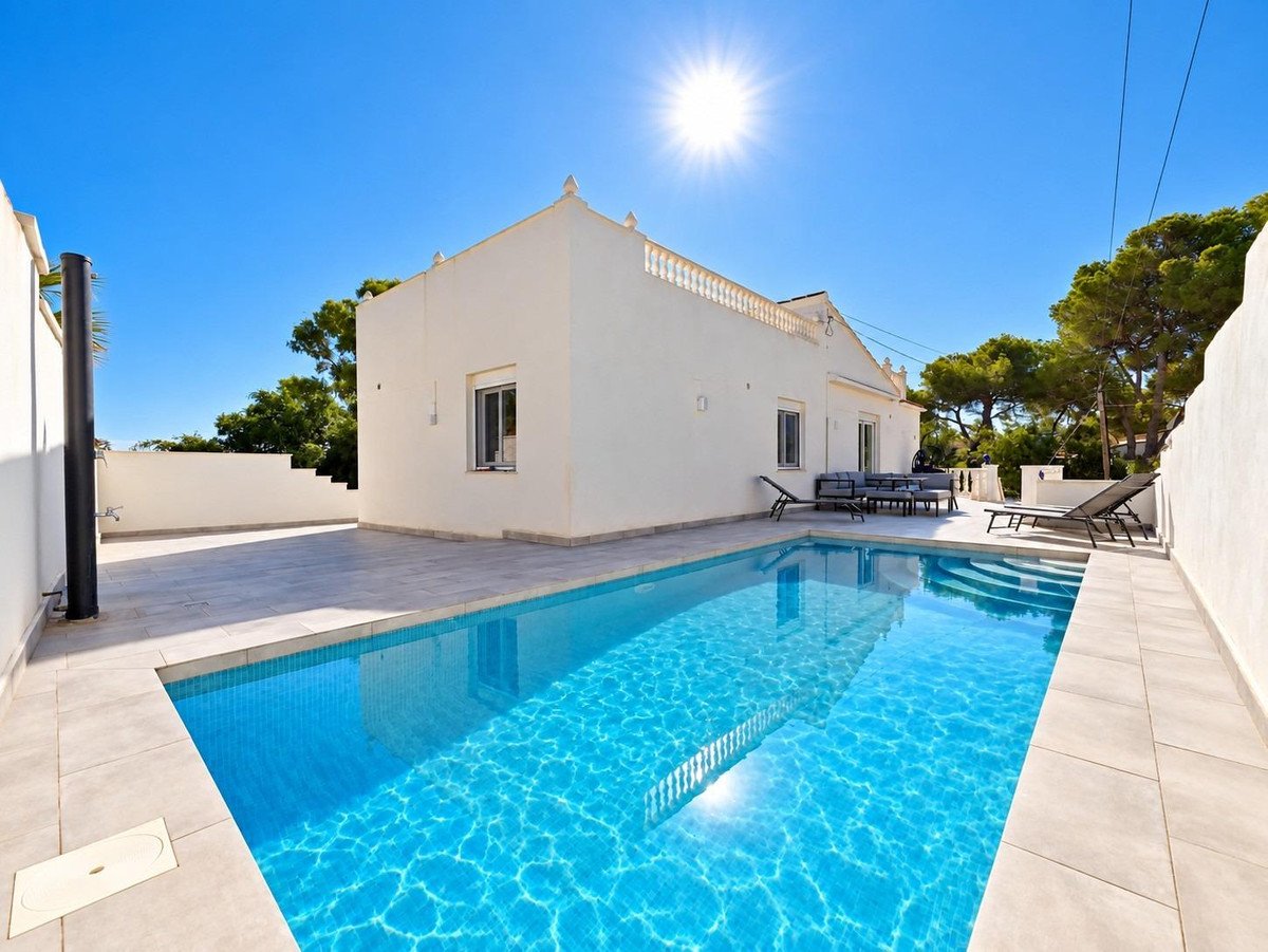 Modern villa with a bright blue swimming pool, outdoor lounge area, and sun loungers under a clear blue sky.