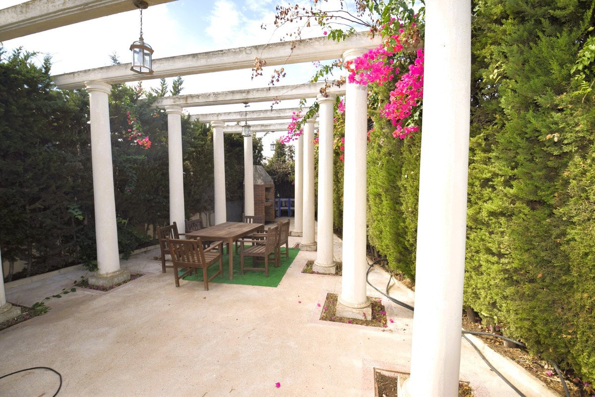 Covered patio with white columns, wooden table and chairs, and pink flowering vines.