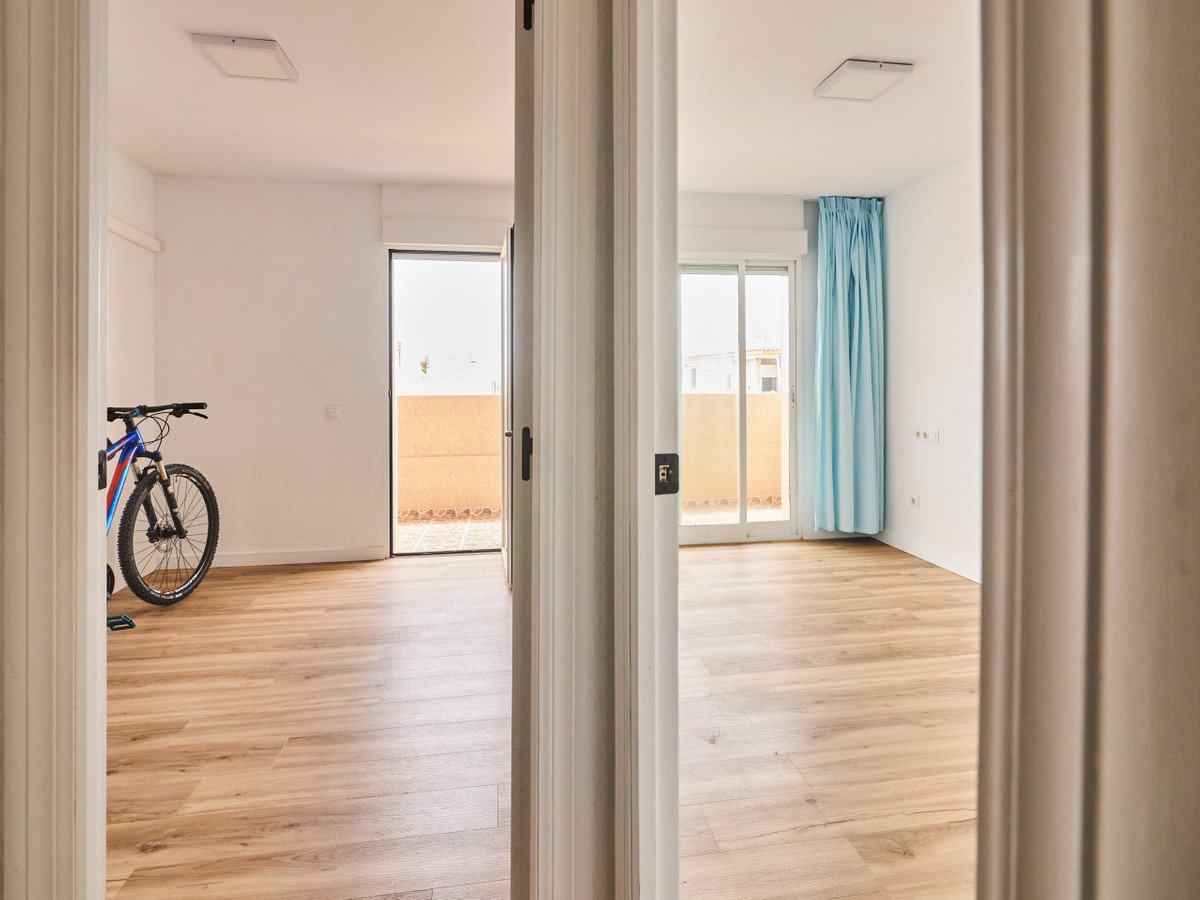 Two bright, unfurnished rooms seen through an open doorway. One room has a bicycle and access to an outdoor patio.