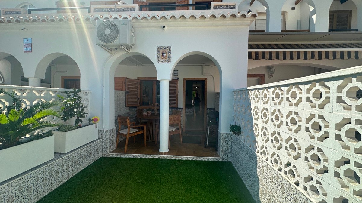 Terraced outdoor patio area with seating, artificial grass lawn, and decorative fencing, featuring an air conditioning unit above.