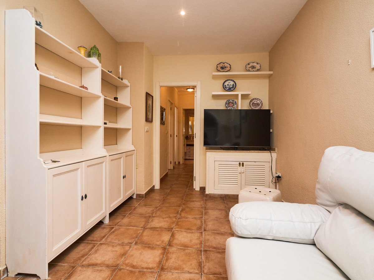 A living room area with a large white shelf, a TV mounted on a cabinet, and a hallway visible in the background.