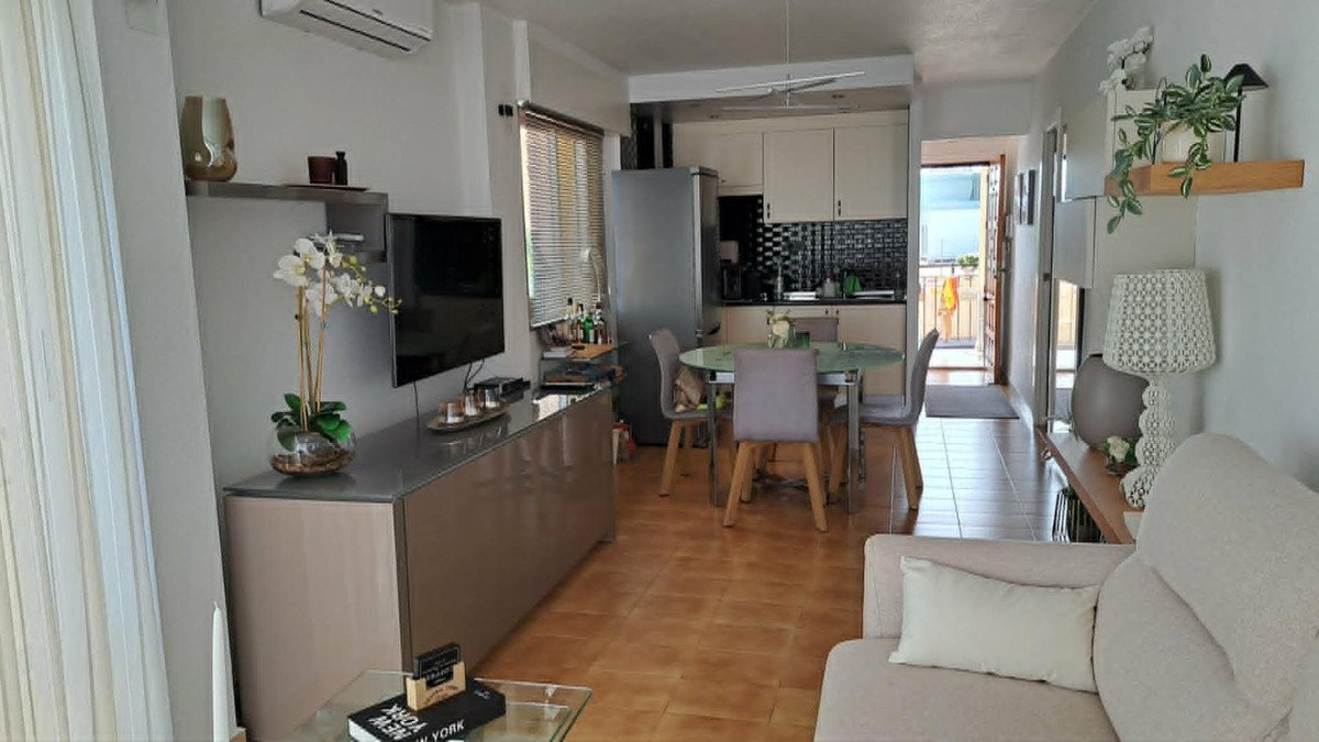 A bright living and dining area with an open kitchen, featuring a TV, dining table, and balcony access visible.