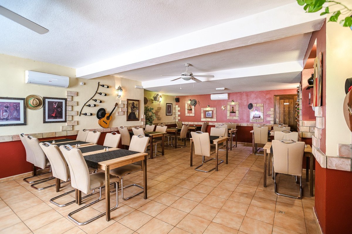 Spanish-themed restaurant dining area with tables, chairs, guitar decor, and red walls.