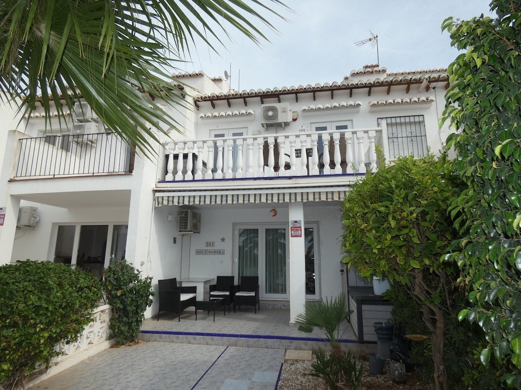 White townhouse with balconies, air conditioning, and an outdoor seating area on the ground floor terrace, surrounded by greenery.