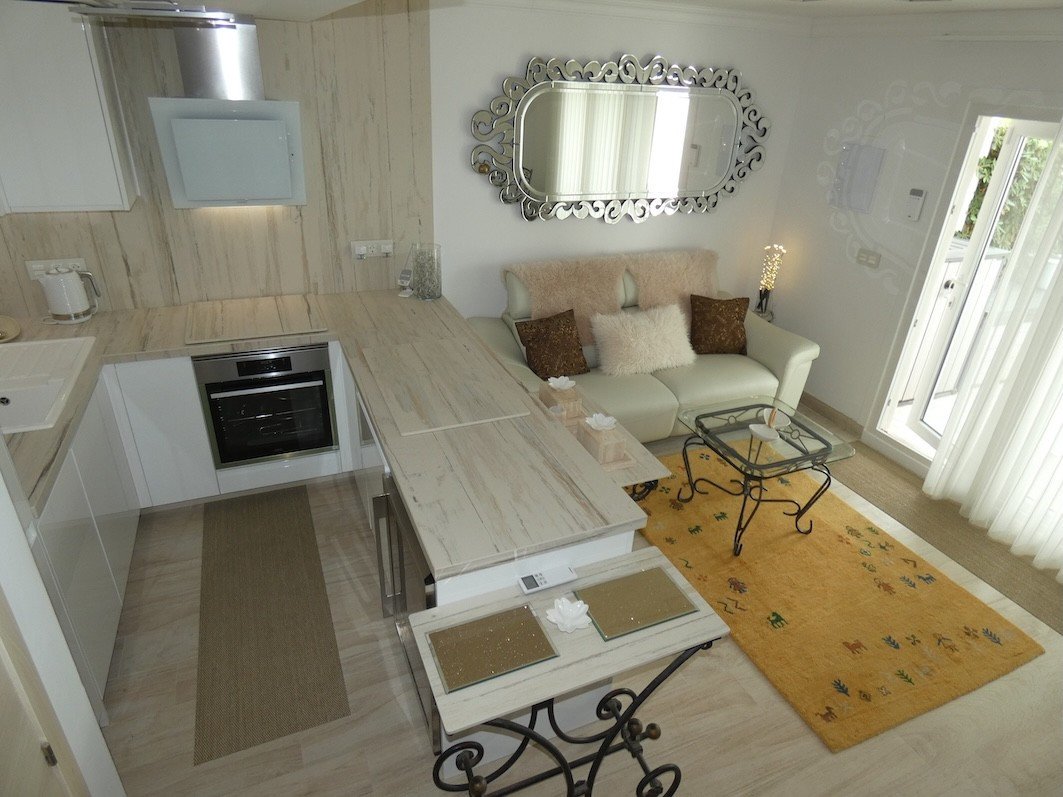 Modern kitchen and living area with a white sofa, glass coffee table, and a yellow rug.