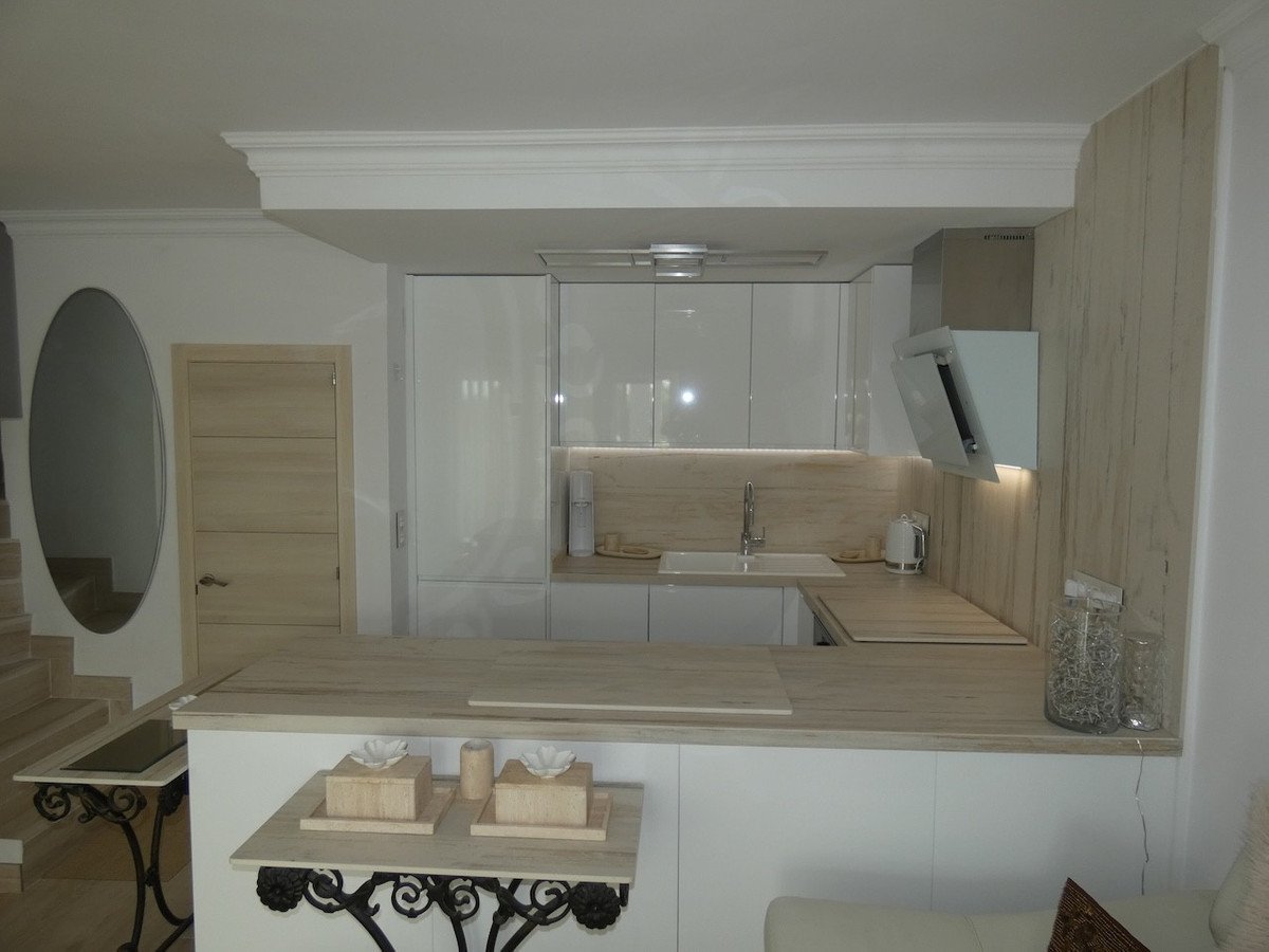 Modern kitchen with white cabinets, a breakfast bar island, and wood accents. Features a sink and stainless steel appliances.