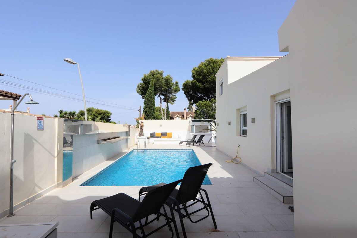 Villa exterior with a private swimming pool, sun loungers, an outdoor shower, and a tiled terrace under a clear blue sky.