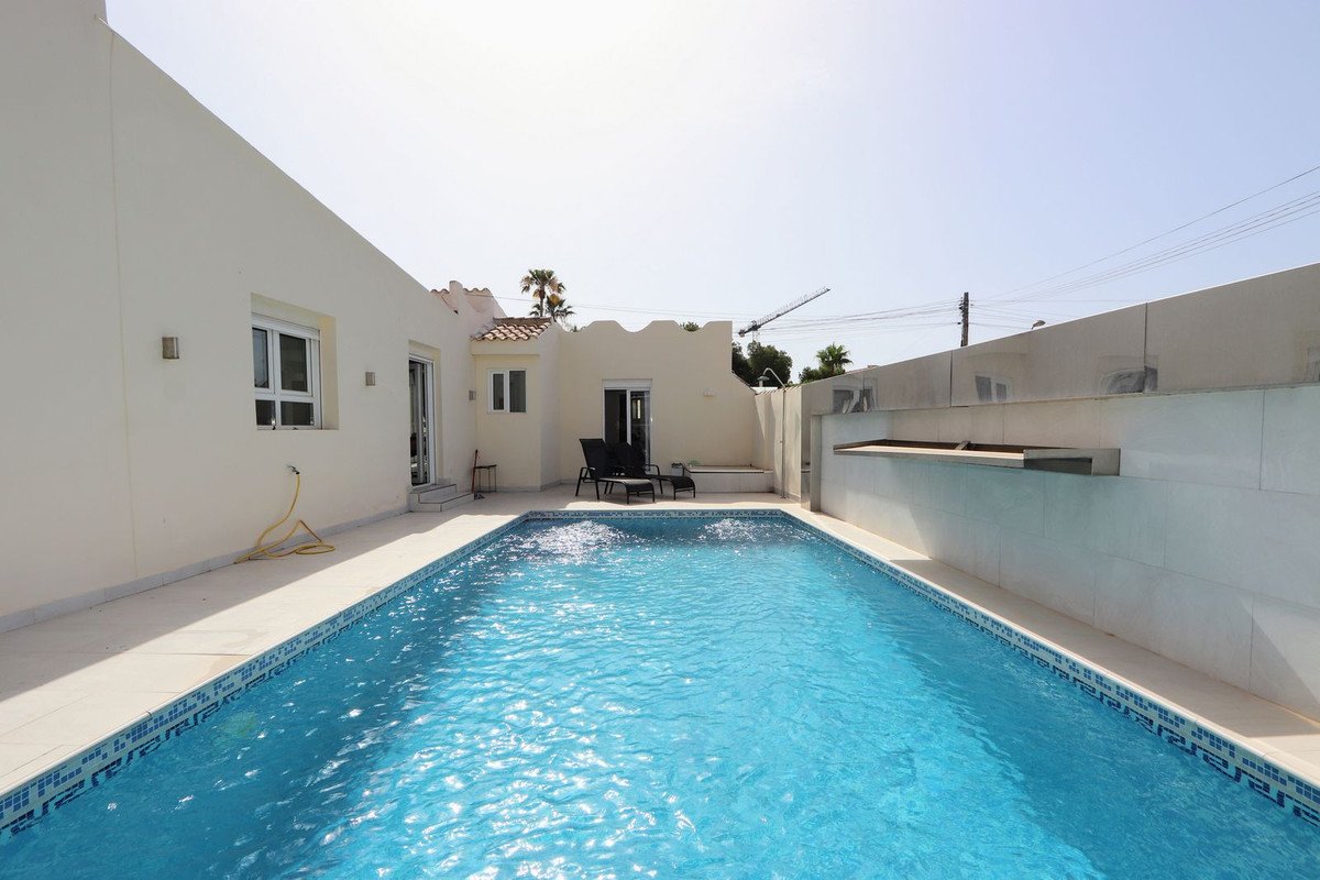 A modern villa with a private blue swimming pool, sun loungers, and a bright sunny sky overhead.