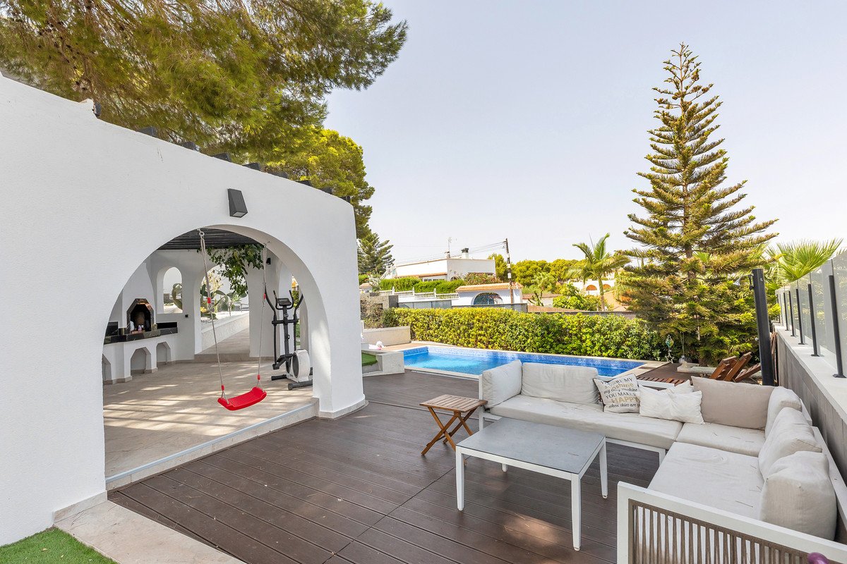 Outdoor patio with a swimming pool, lounge seating, BBQ area, and exercise equipment, featuring lush greenery and trees.