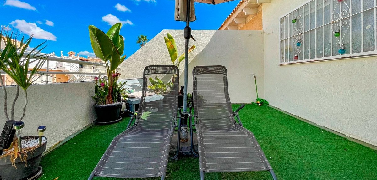 Terrace with two lounge chairs, plants, and an umbrella under a blue sky.