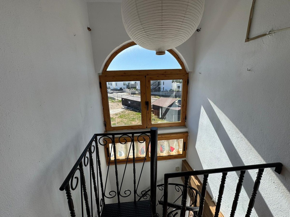 Interior view of a staircase with a wooden window showing an outdoor view with buildings and blue sky.
