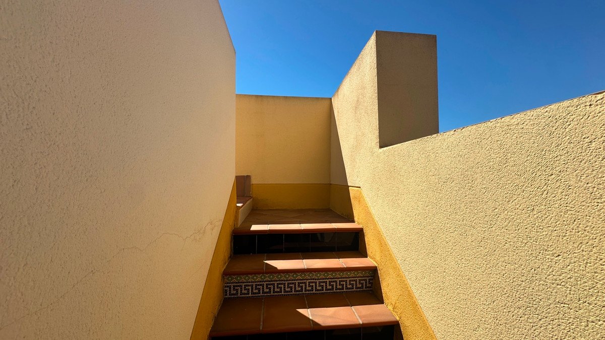 Exterior staircase with terracotta tiles and decorative border, leading up towards a clear blue sky.