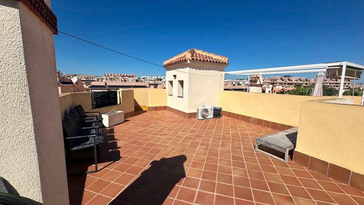 A spacious tiled terrace with outdoor seating, a small structure, and an air conditioning unit under a clear blue sky.