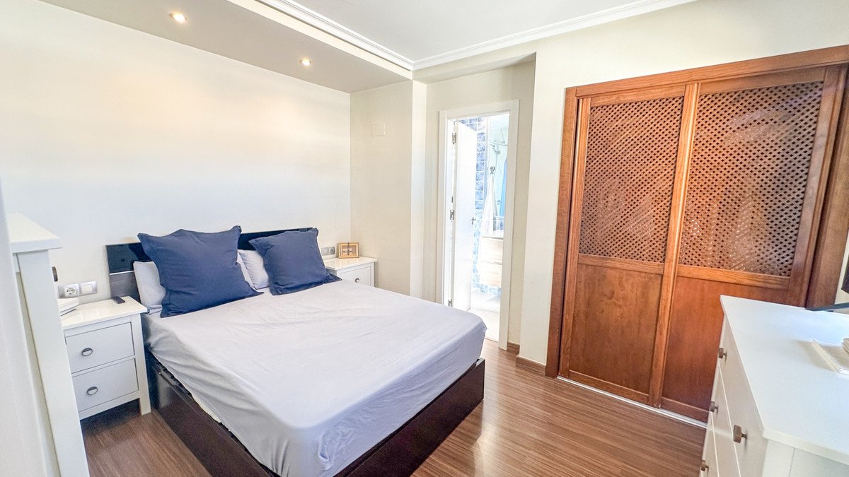 A bedroom with a double bed, blue pillows, wooden wardrobe, and a door opening to a balcony.