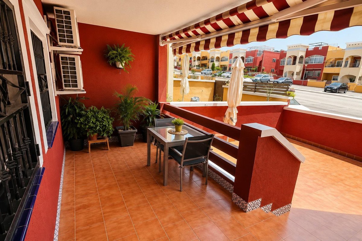 A terrace with outdoor seating, potted plants, and a striped awning overlooking colorful buildings and a street.