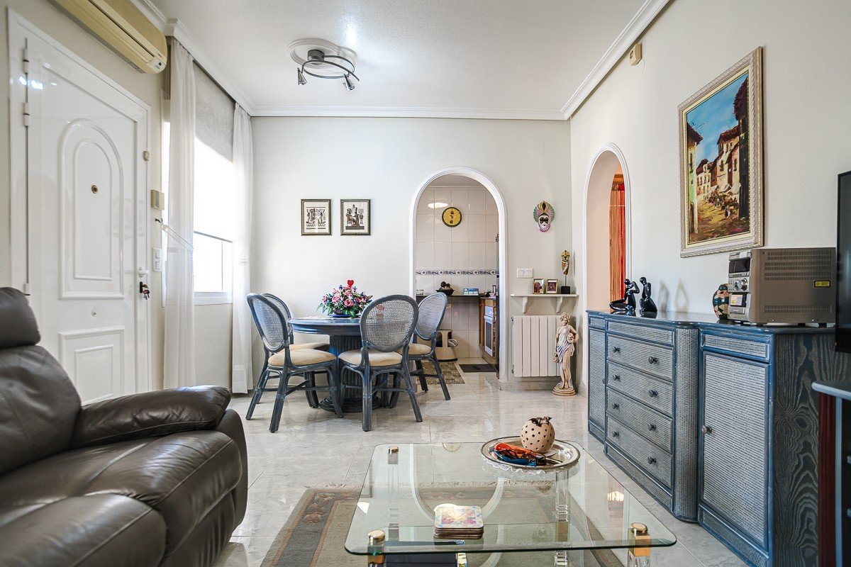Interior of a living and dining area with a leather sofa, dining table, and decorative furniture. An archway leads to the kitchen.