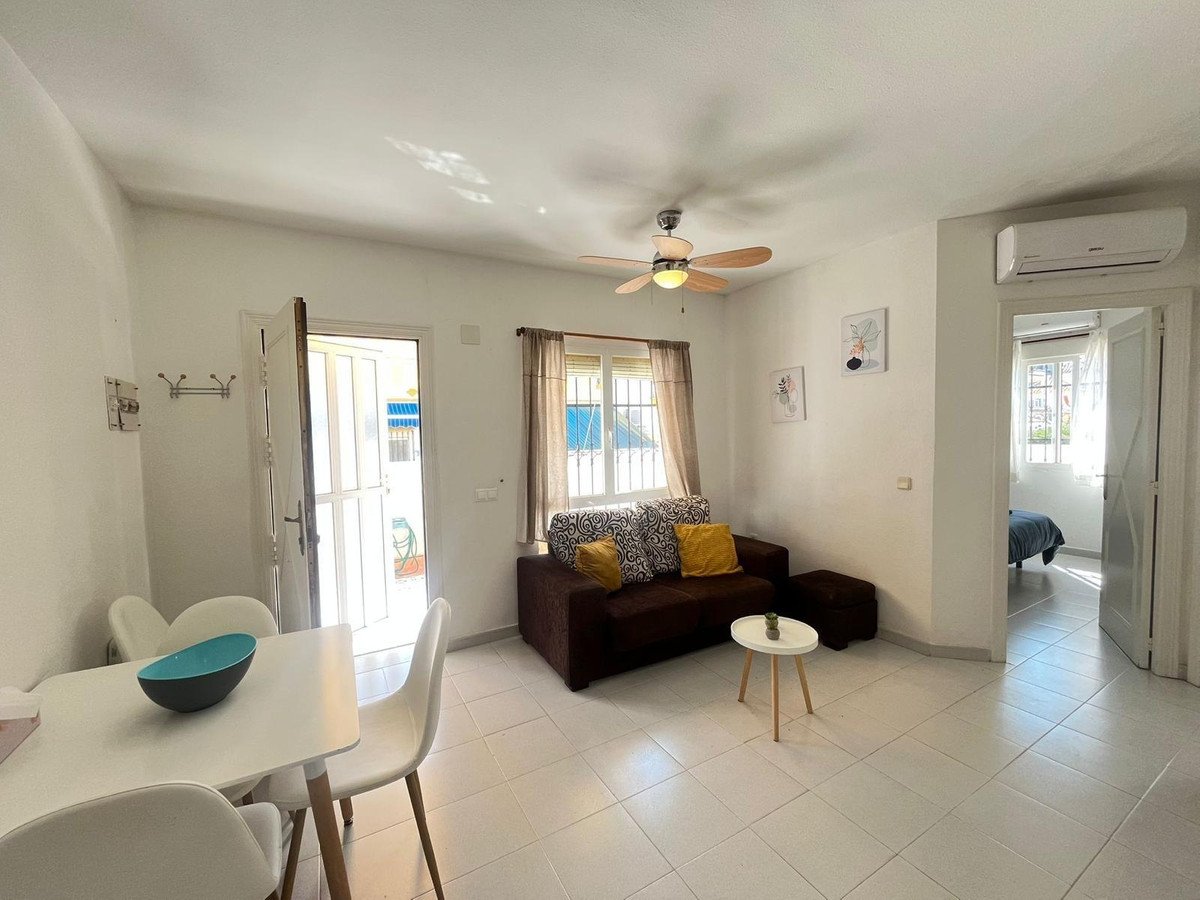 Living area with sofa, dining table, and view into a bedroom, with a door leading to a terrace.