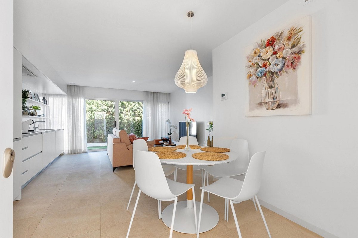 Modern open-plan dining and living area with white furniture, large windows, and a floral painting.