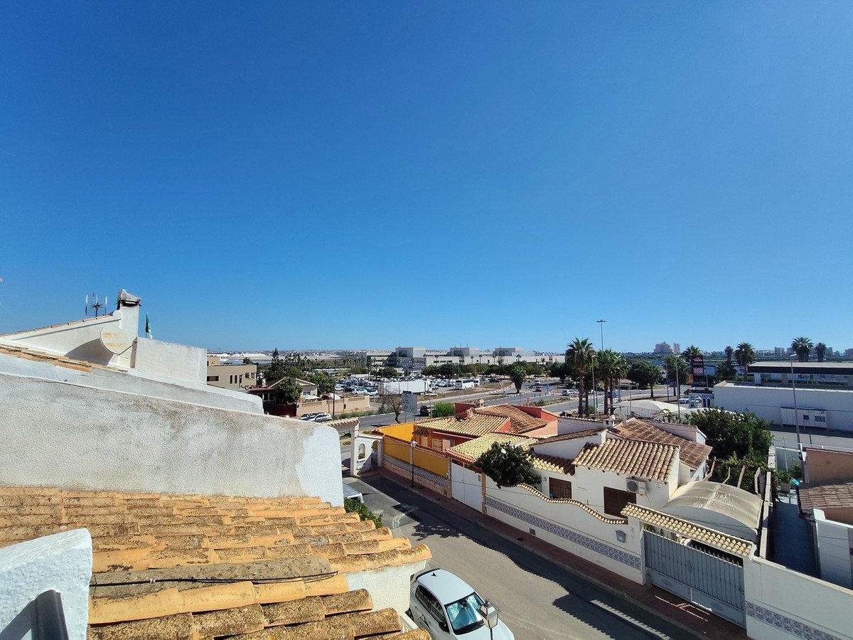 View from a rooftop of houses, a street, and distant buildings under a clear blue sky.