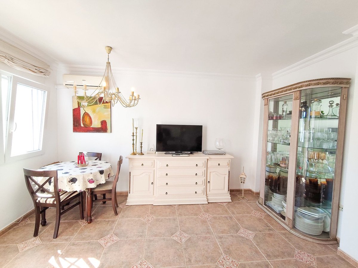 Interior view of a dining and living area featuring a small dining table, a TV, a cabinet, and artwork.