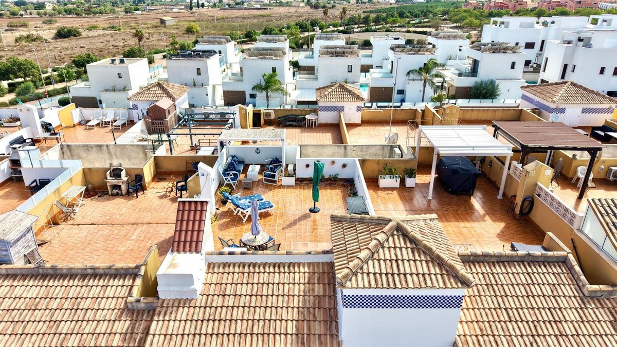 Spacious rooftop terrace with lounge seating, dining area, awnings, and views of surrounding white buildings and landscape.