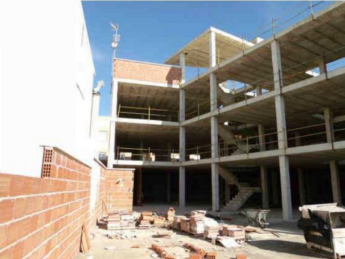 Exterior view of a multi-story building under construction, with concrete floors and brick walls, under a clear blue sky.