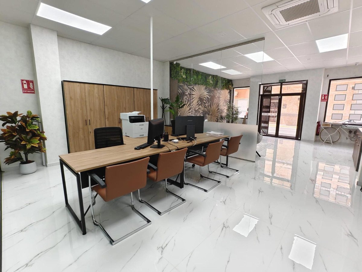 Modern office space with a wooden desk, brown chairs, and a view of the entrance.