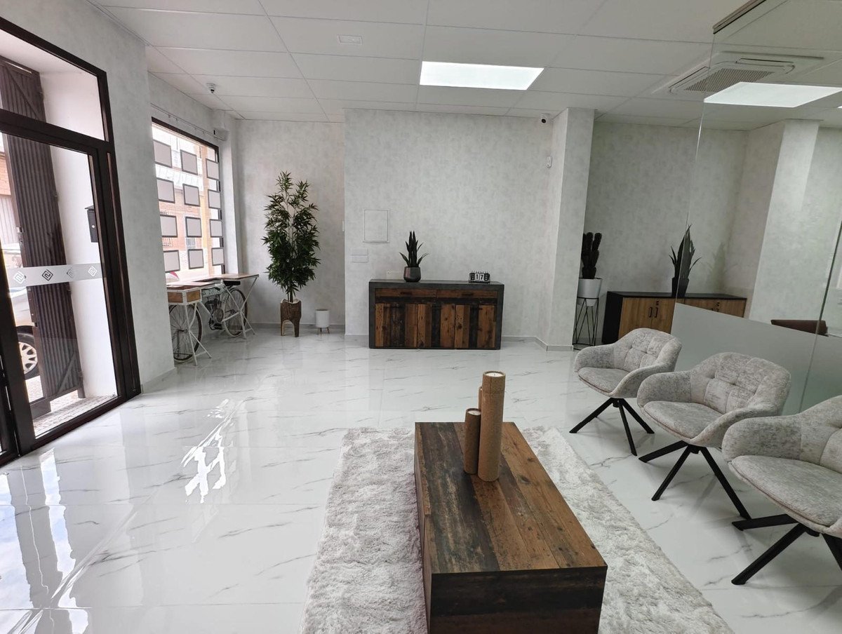 A modern reception area with comfortable seating, decorative plants, and a wooden coffee table on a plush rug.