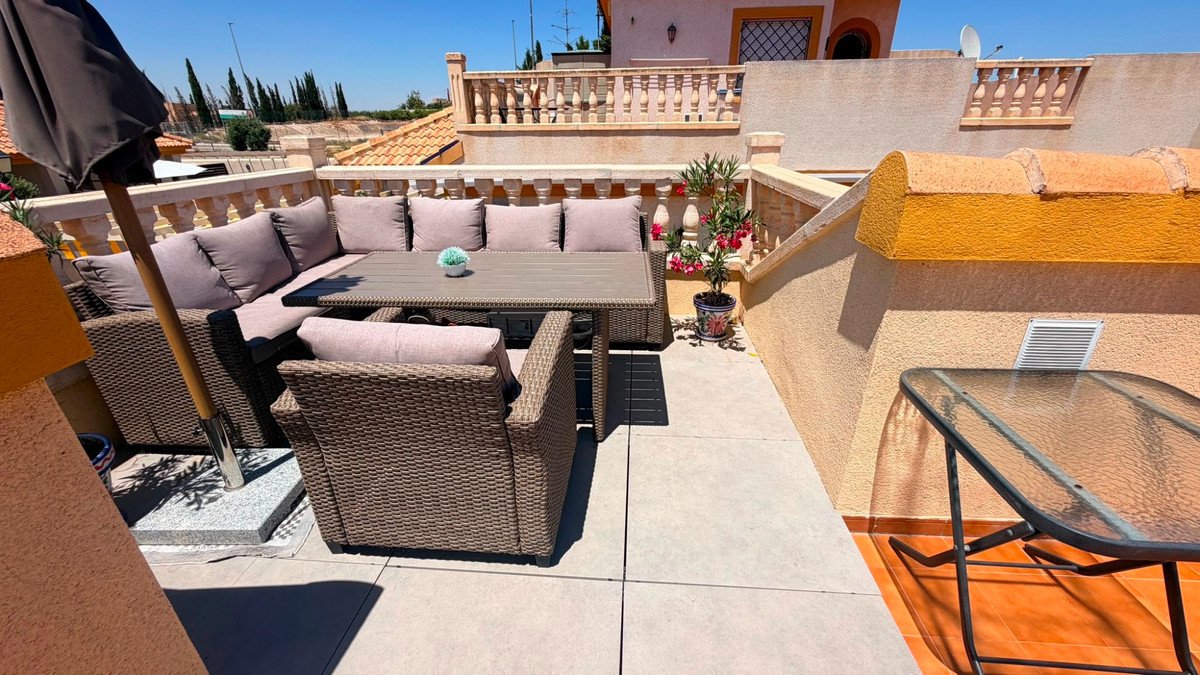 Rooftop terrace with wicker seating, table, and outdoor furniture under sunny sky