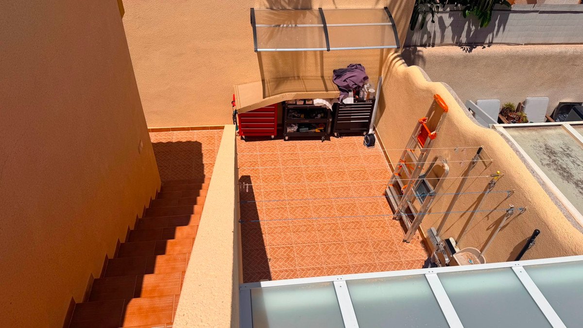 A sunny terrace with tiled flooring, storage items, and stairs leading down.