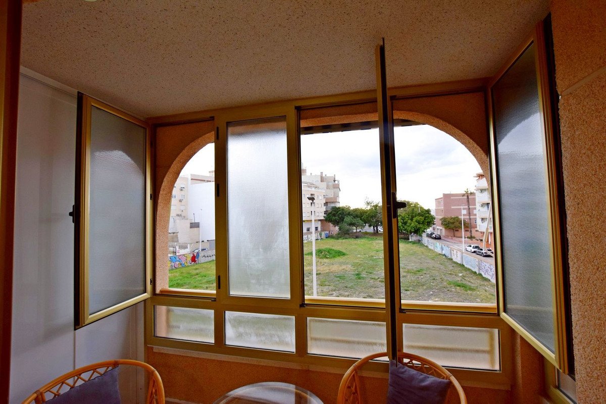 View from a balcony with large windows and arched openings, overlooking a grassy field and buildings.