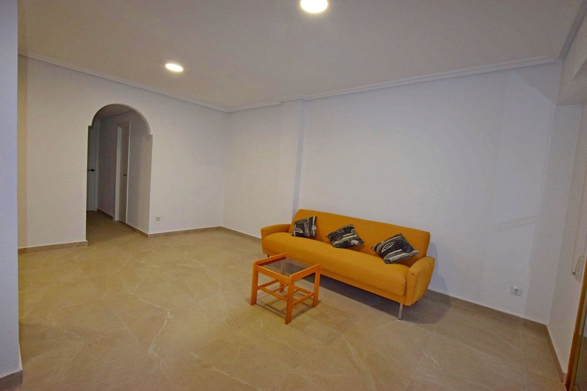 Spacious living room with an orange sofa and decorative pillows, featuring a marble floor and an arched doorway leading to another room.