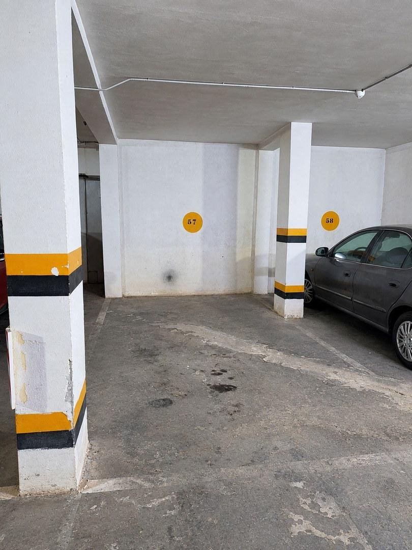 Underground parking space marked with number 57, with a grey car parked in the adjacent bay. Concrete floor and pillars.