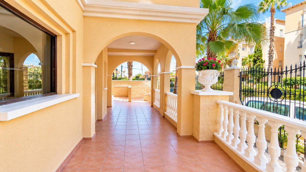 A covered terrace with arches, balustrade, and a view of palm trees and buildings.