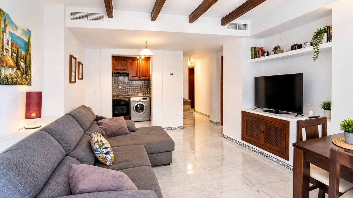Modern living room with a large sectional sofa, kitchenette, television, and dining area. Features exposed beams and bright decor.